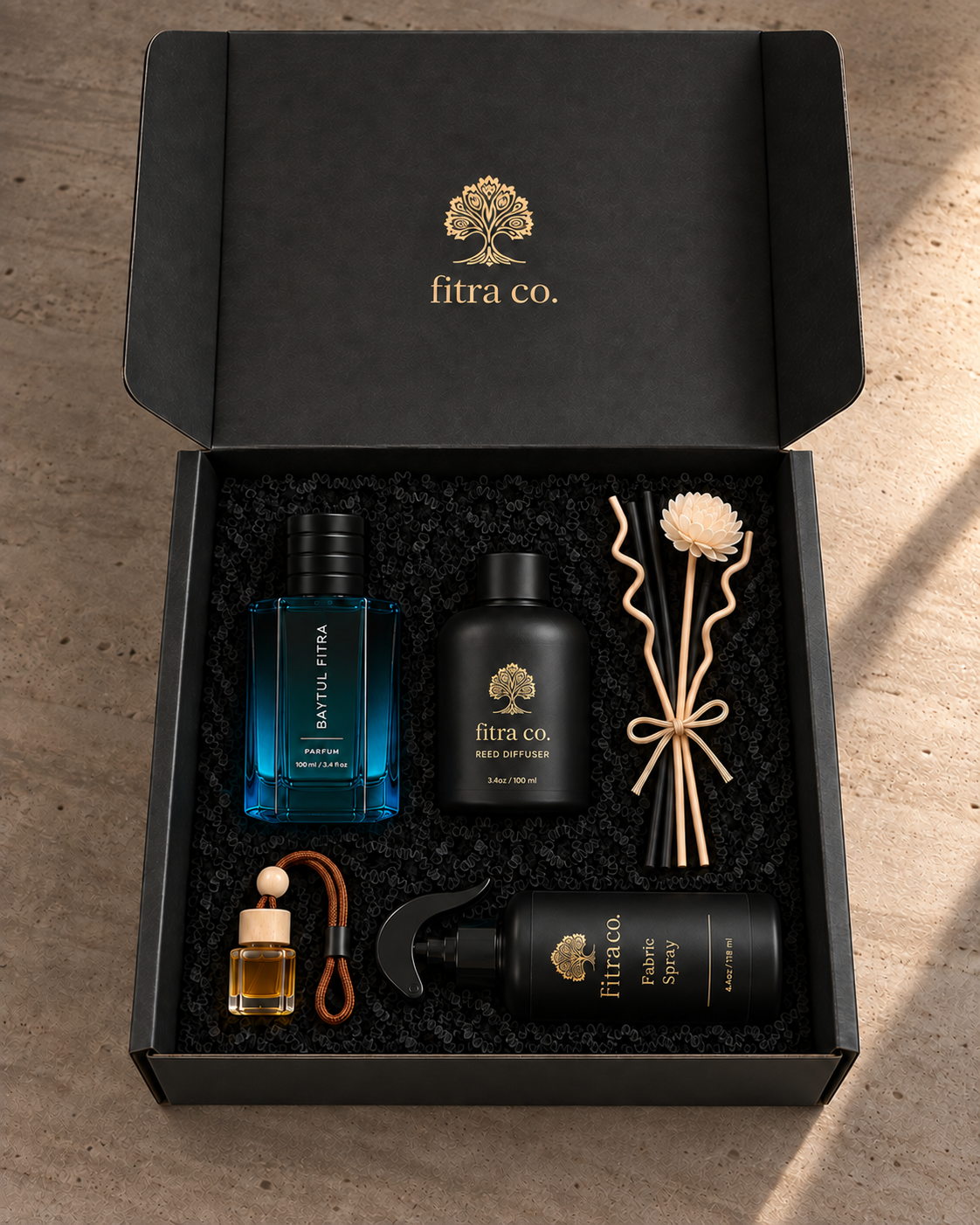 Four products in the open Fitra Plus Gift Set, with a full-length lid and ribbon-tied black reeds, curly reeds and cream flower beside the home diffuser.